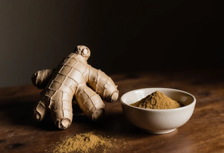 Fresh ginger root and a bowl of golden ginger powder on a wooden counter