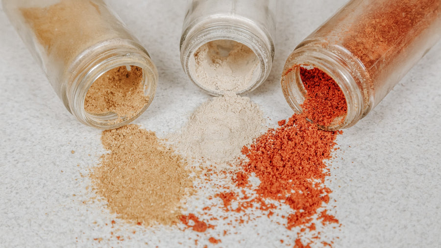 Glass spice jars and small mounds of colourful ground spices on a pale surface