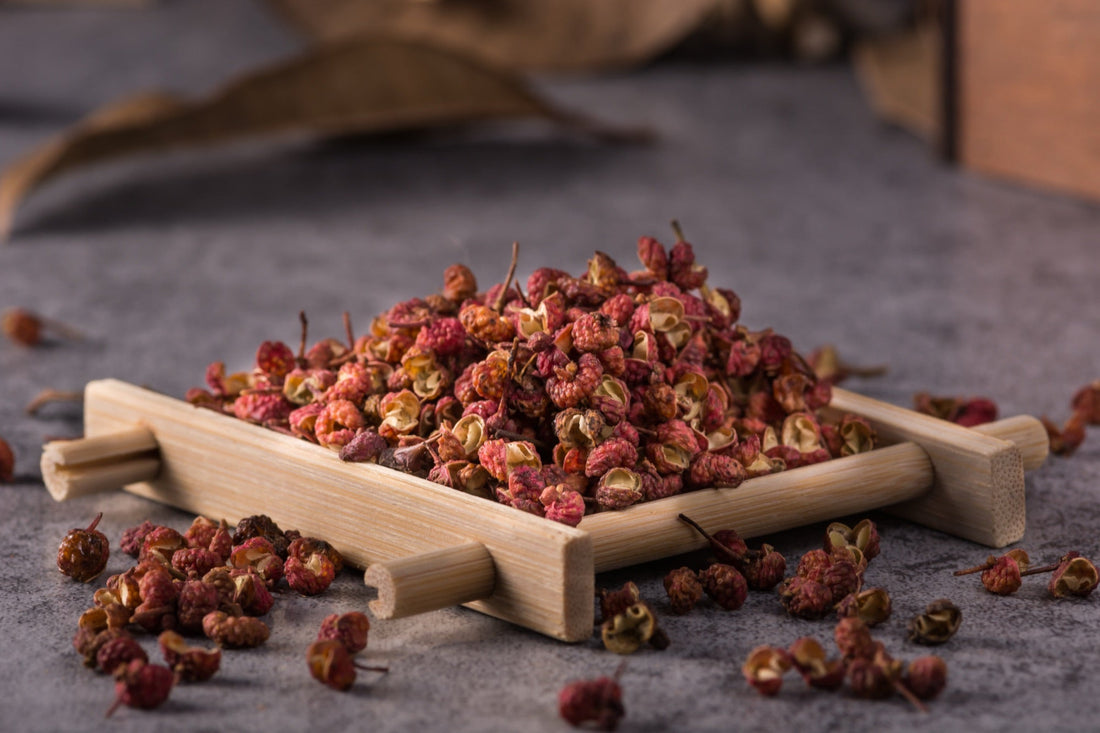 Sun-dried Sichuan peppercorns (jaiur) in a small wooden tray with scattered peppercorns around it