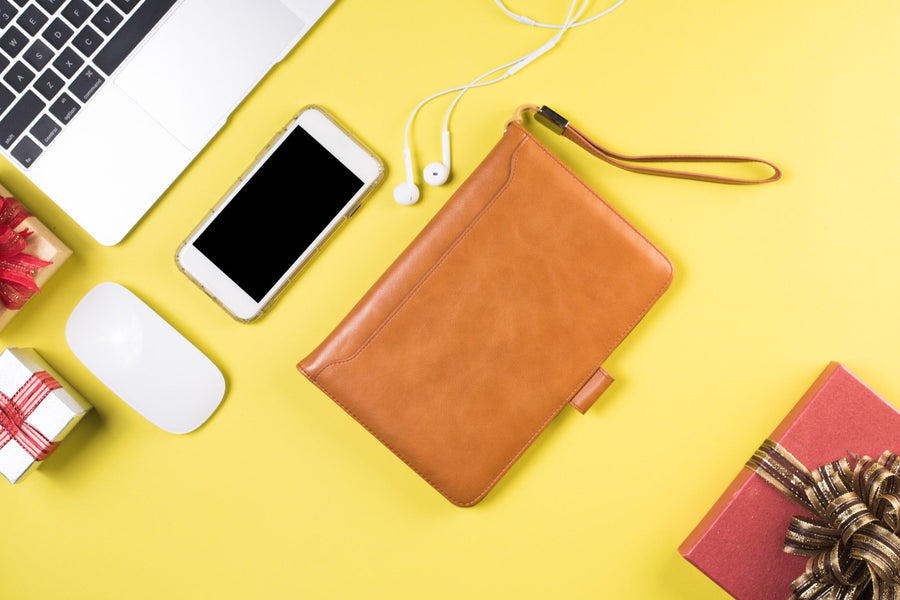 Flat-lay of a tech pouch packing setup — leather pouch, phone, earphones, laptop edge on a yellow surface
