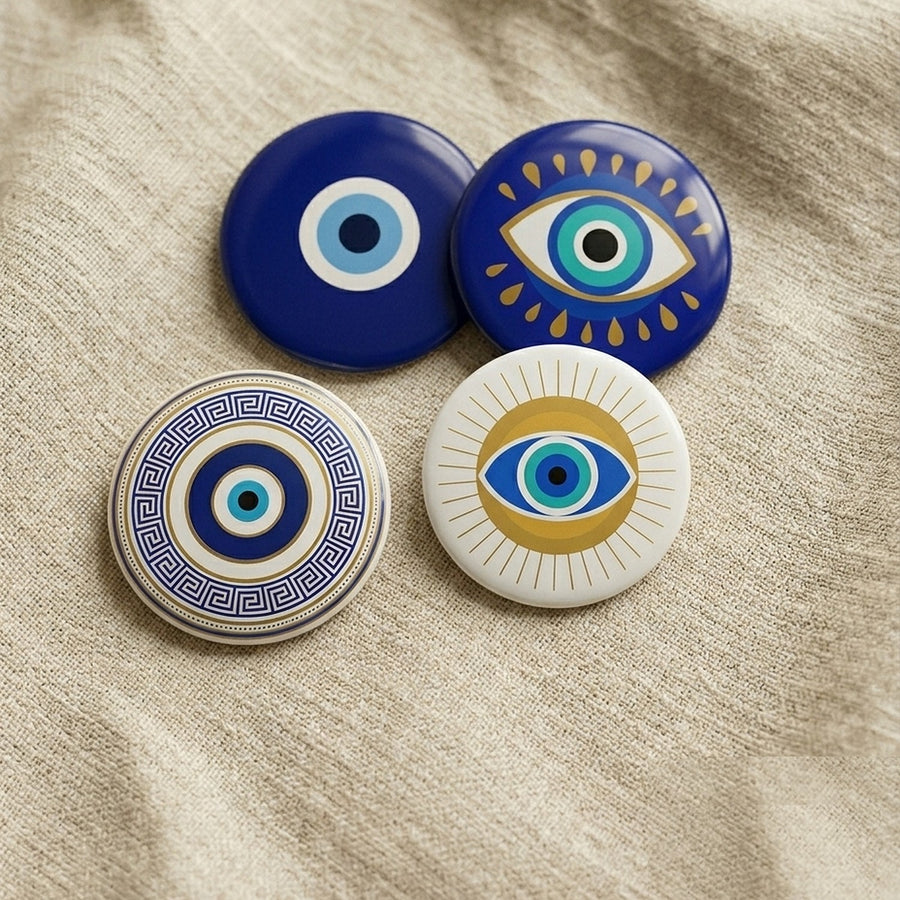 Four hand-finished evil-eye pin badges arranged on warm cream linen — the Rochcha set of four different nazar designs.