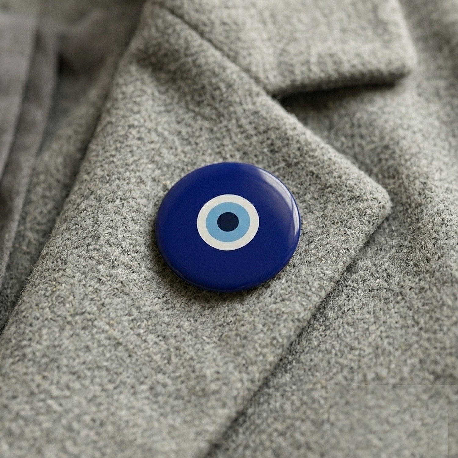 A classical navy nazar pin badge worn on a heathered grey wool coat lapel.
