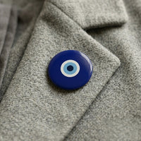 A classical navy nazar pin badge worn on a heathered grey wool coat lapel.