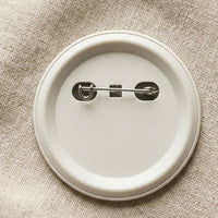 Back of a Mawlaii Rochcha pin badge — matte off-white plastic shell with stainless steel pinback hardware.