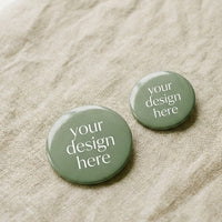 Two sage green Custom Print Badges from Mawlaii Rochcha on warm linen — 44mm and 58mm, glossy laminated finish, ready for your artwork.
