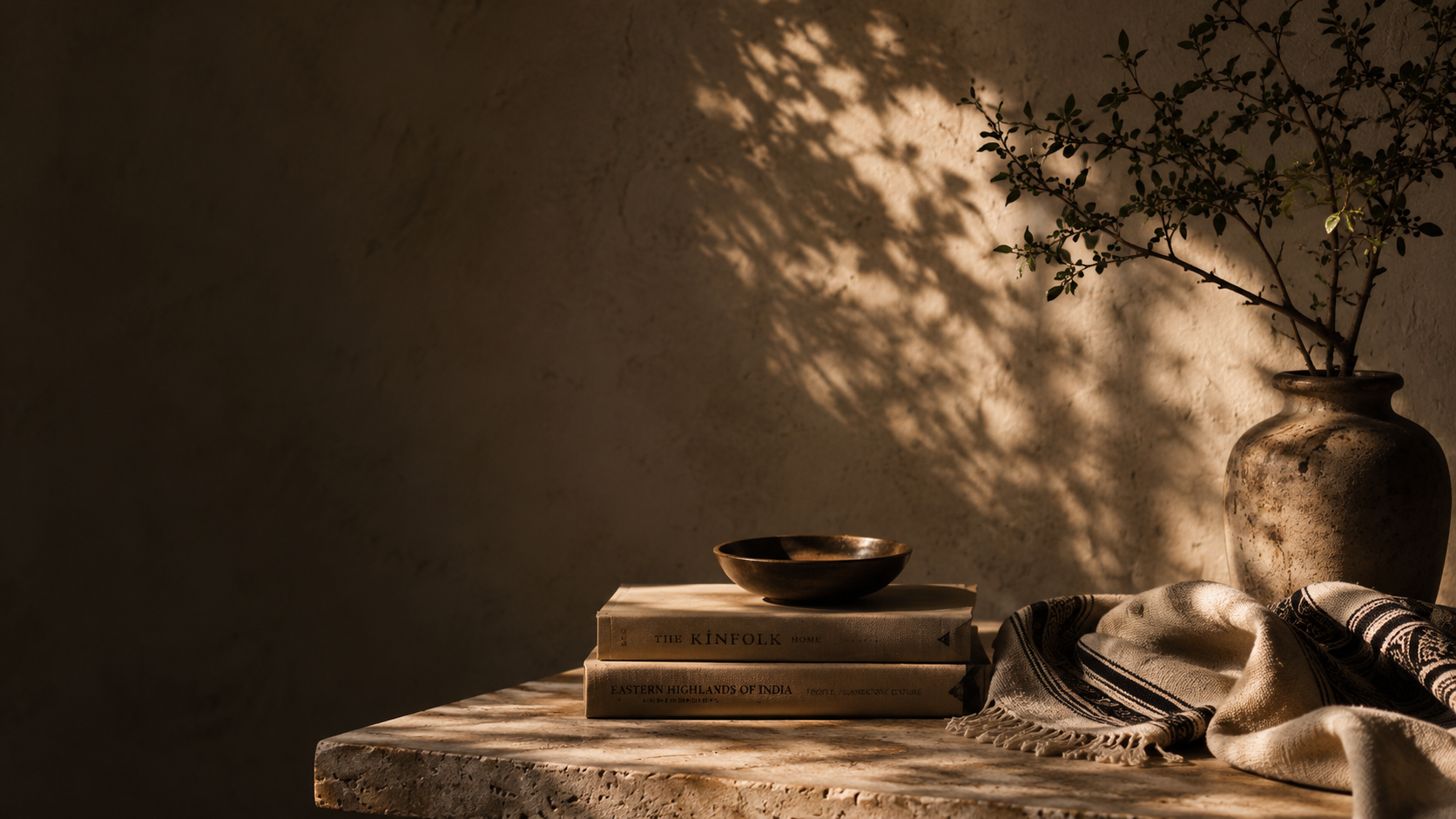 Mawlaii hero — still-life with ceramic vase, brass bowl on stacked books, handwoven textile, against a cream plaster wall in afternoon light