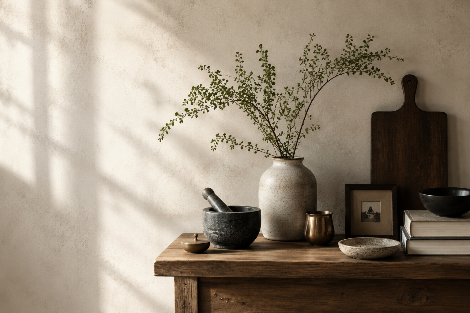 Mawlaii — a still-life of curated objects on a wooden table: ceramic vase with branches, mortar and pestle, brass vessel, and books